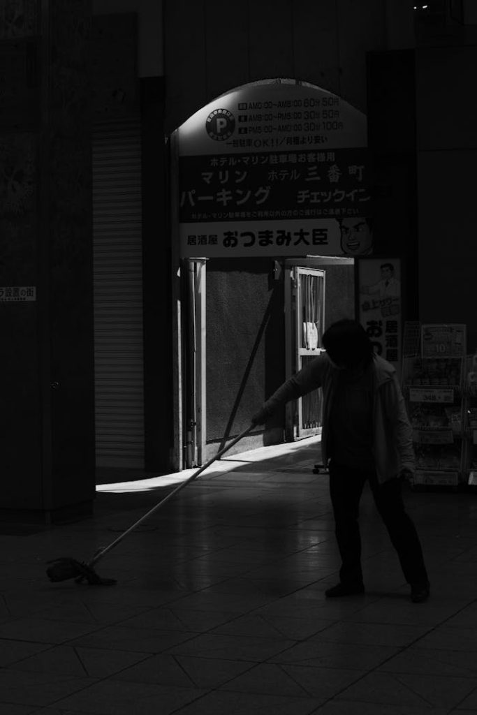 Black and white silhouette of a person cleaning indoors in dim lighting.