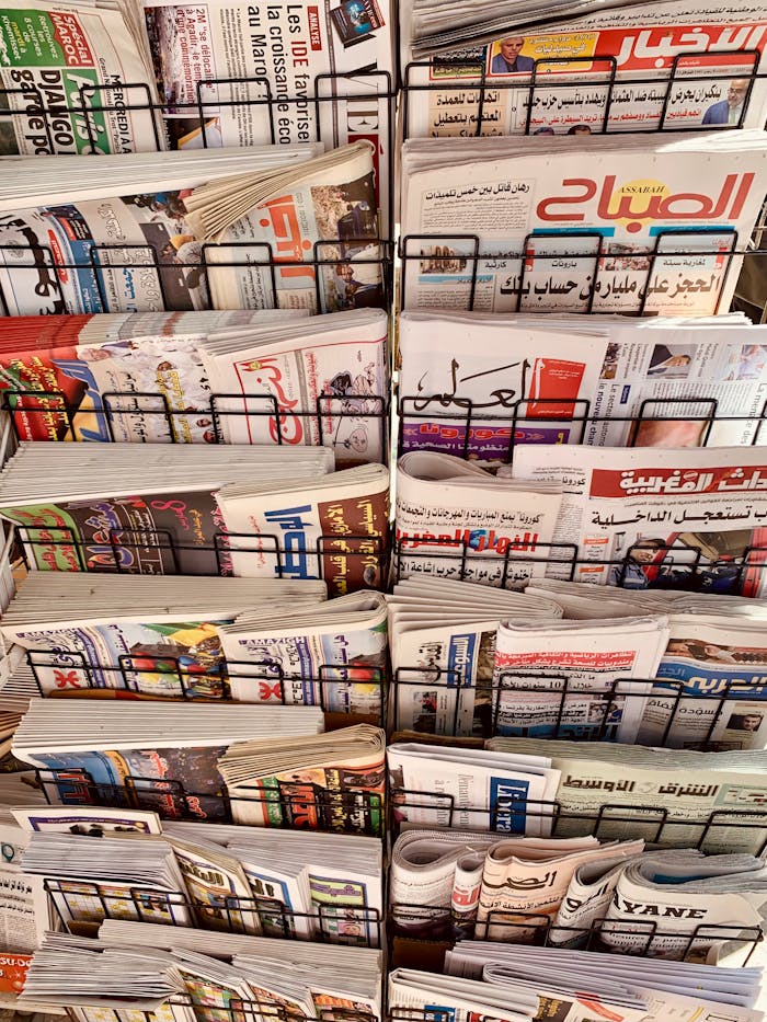 A diverse collection of newspapers in various languages displayed on a metal stand.
