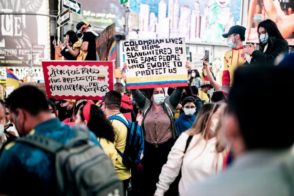 Protesters in Times Square advocating for Colombian lives and justice, featuring face masks and placards.