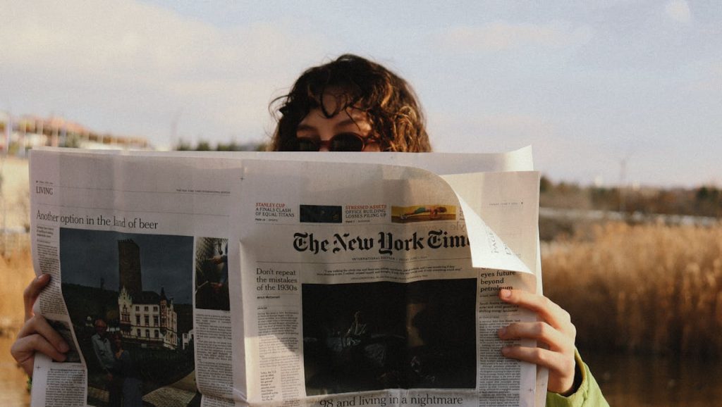 A person reads The New York Times outside on a sunny day, capturing a moment of leisure.